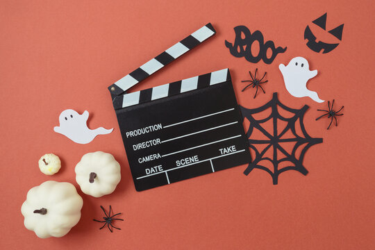 Horror movie night and Halloween party concept with white pumpkin, decorations and movie clapperboard on modern background. Top view, flat lay