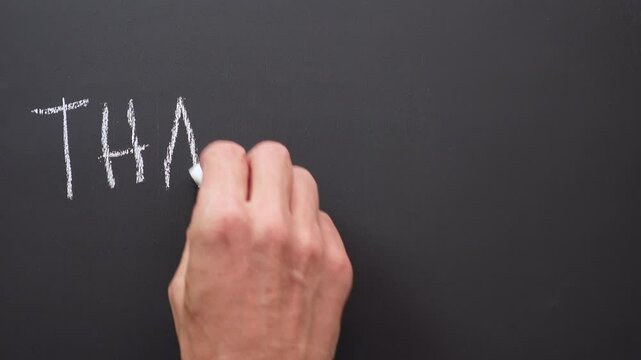 A hand writes the words or expression &ldquo;thank you&rdquo; with white chalk on a black board
