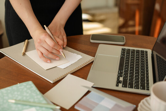 Close-up of a woman standing at her desk writing on a piece of paper