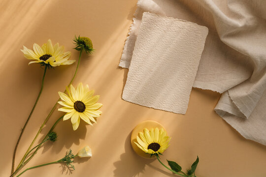 Blank piece of deckle edge card on a table with assorted yellow flowers and a piece of fabric