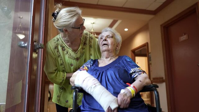 Closeup of elderly woman with cast on broken arm and black eye hematoma in wheelchair with woman family member talking to her.