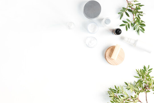 Overhead view of glass cosmetic bottles, a brown glass cosmetic dropper bottle for face serum or oil and pistachio branches on a white background