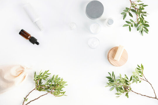 Overhead view of glass cosmetic bottles, a brown glass cosmetic dropper bottle for face serum or oil and pistachio branches on a white background
