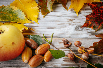 Rustic autumn arrangement with acorns and vibrant fallen leaves in shades of yellow, brown and orange on a weathered wooden surface. The composition reflects the essence of autumn with natural texture