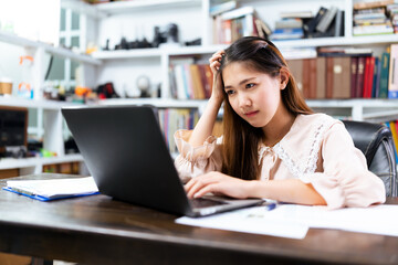 Beautiful asian businesswoman working at home office using computer laptop technology, home office work desk, working on computer feeling stressed out anxious confused, with bookshelves background.