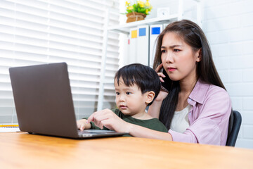 Asian businesswoman working in modern office while looking after child,teaching working and being a family care motherhood raising her kid while working with computer laptop technology