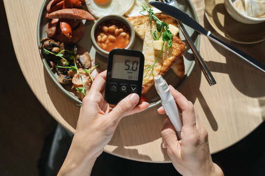 Close-up overhead view of a woman holding a glaucometer (glucometer) and flash glucose monitor to check her sugar levels before breakfast