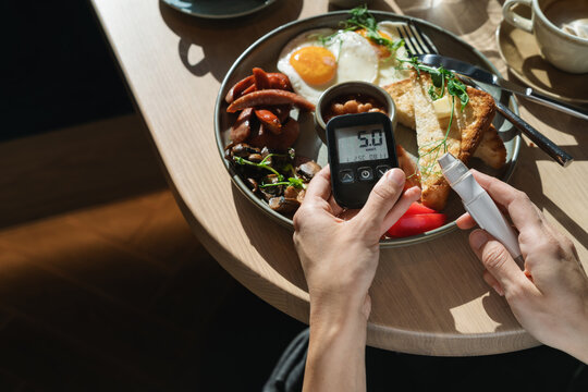 Close-up overhead view of a woman holding a glaucometer (glucometer) and flash glucose monitor to check her sugar levels before breakfast