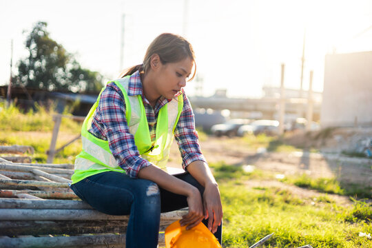 Asian female working in construction sitting resting tired exhausted, working building innovation on architecture, wearing safety vest and helmet gears.