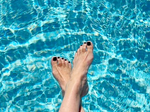 Overhead view of a woman sitting at the edge of a swimming pool dangling her feet in the water