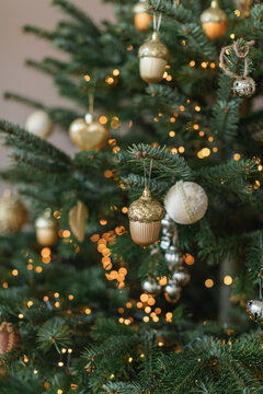 Close-up of assorted gold Christmas ornaments on a Christmas tree with fairy lights in a living room