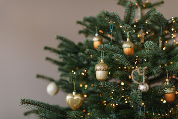 Close-up of assorted gold Christmas ornaments on a Christmas tree with fairy lights in a living room