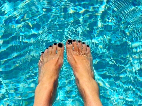 Overhead view of a woman sitting at the edge of a swimming pool dangling her feet in the water