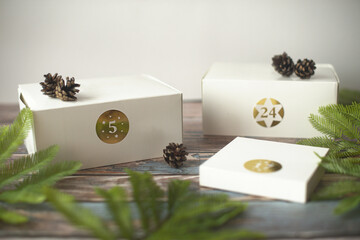 Gift boxes for a Christmas advent calendar with pine branches and pinecones on a wooden table