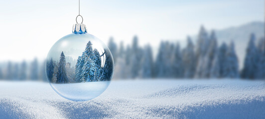 Weihnachtskugel aus Glas vor verschneiter Landschaft im Hintergrund