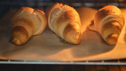 Three croissants baking in the oven on parchment paper. Close-up food photography of pastry baking...