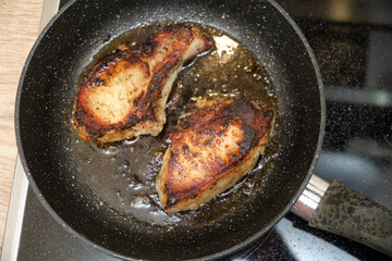 Two pieces of cooked pork meat in a frying pan. Close-up top view of grilled meat on a stovetop