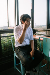 A Southeast Asian man sitting on a chair, holding his head with both hands