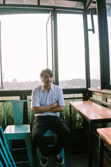 A Southeast Asian man sitting on a chair with his arms crossed