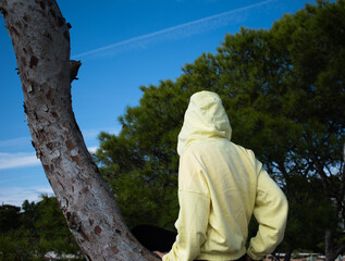 Person in yellow hoodie sits on a tree trunk, enjoying tranquil moment in nature