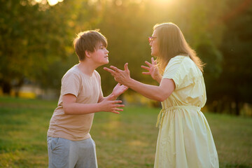 Mother arguing with teenage son outdoors in a park during sunset. Family conflict and communication...