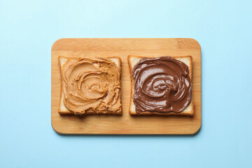 Delicious sandwiches with peanut butter and chocolate paste on light blue table, top view