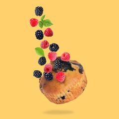 Delicious muffin and berries in air on golden background