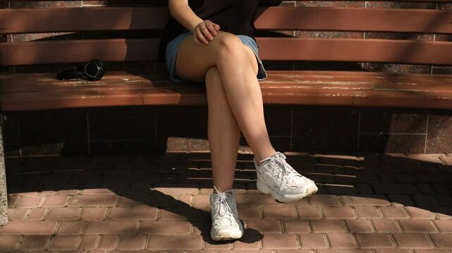 young woman taps her foot to the beat of the music while sitting on a bench on a sunny summer day, close-up of her foot