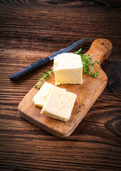 Fresh French sea salt butter garnished with thyme offered as close-up on a rustic wooden chopping board