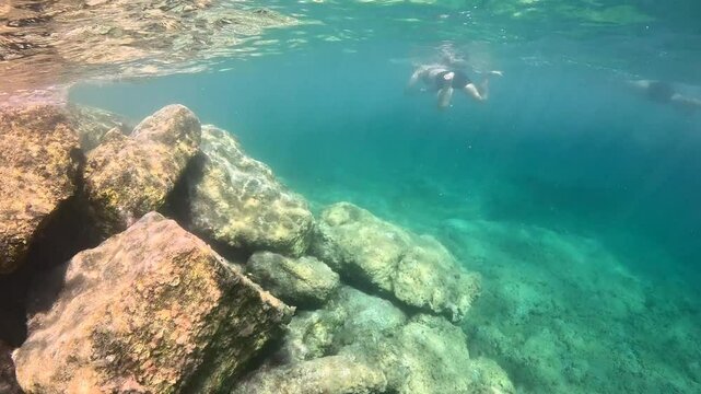 People snorkeling in the shallow sea with fish and big stones. Seascape with rocks and swimming tourists. Blue green ocean, marine life in the water. Travel video from snorkeling trip.