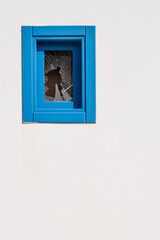 a small window with a blue wooden frame with a broken glass, on a white facade, copy space, negative space, rule of thirds, vertical