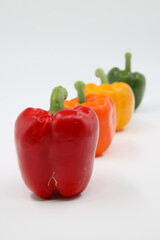  Four bell peppers in red, orange, yellow, and green, arranged in a diagonal line on a white background.
