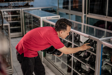 male asian employee arranges black leather shoes in display case