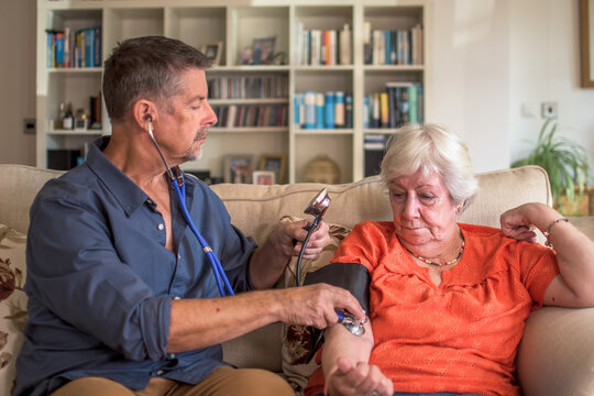 A doctor, physician takes a patients blood pressure at a home visit, healthcare call. Hypotension, stroke, senior care prevention check up. social, residential and nursing home appointment.