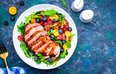 Foodie food salad with grilled duck and bloody orange, kumquat, blueberry and lettuce on blue background, top view