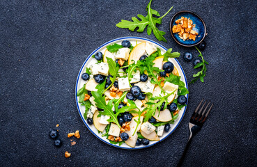 Tasty salad with pears, blueberries, roquefort cheese, arugula and nuts. Black background, top view
