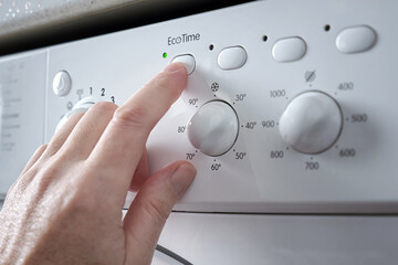 Close-up of a man's hand pressing the button for selecting the economical washing mode on the panel of the washing machine.