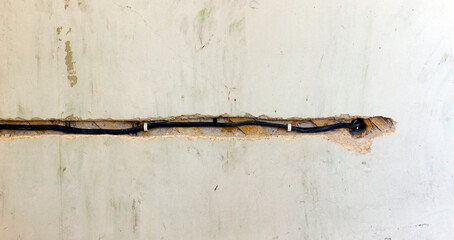 Exposed electrical wiring embedded in damaged wall, showing signs of wear and potential safety issues.