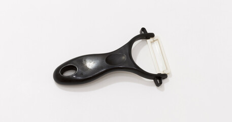 Black plastic vegetable peeler with white ceramic blade on plain white background.