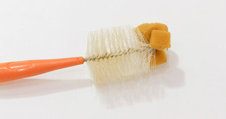 Old bottle brush with orange plastic handle, worn bristles, and attached sponge for cleaning hard to reach areas.