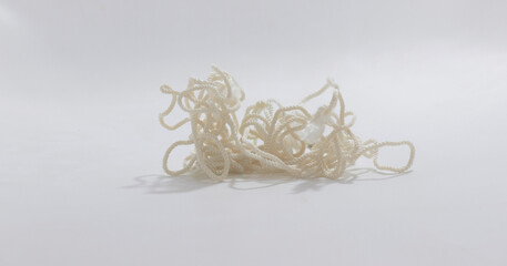 Tangled white rope on plain background, casting soft shadows, representing chaos, confusion, or...