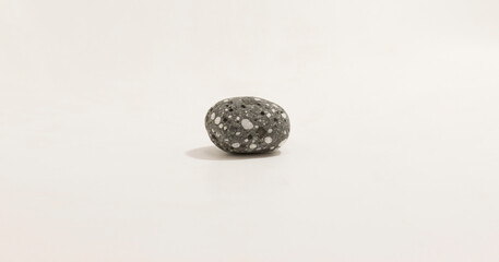 Smooth gray stone with white speckles on plain background, isolated and minimalistic in natural lighting.
