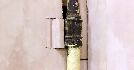 Close up of rusty iron pipe emerging from wall with poorly cut plasterboard revealing the pipe.