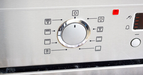 Stainless steel oven control panel with various cooking symbols and central knob for mode selection.