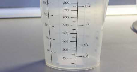 Plastic measuring cup with metric and fraction markings for precise liquid measurements, ideal for cooking and laboratory use.
