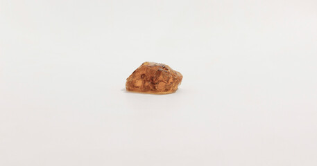 A single small, irregularly shaped amber colored gemstone on smooth, neutral background.