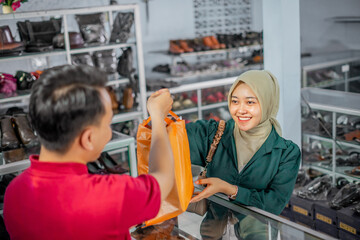 Fototapeta premium high angle view of hijab customer taking purchased product from leather shoes store male staff