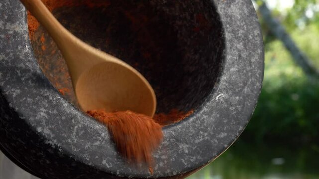 Small bamboo spoon is taking a mix of spices and peppers from the grey stone mortar on the background of the pond . High quality 4k footage