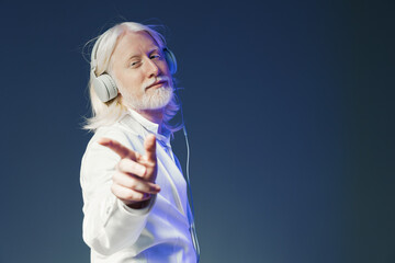 Senior man with headphones enjoying music, smiling and posing confidently against a gradient blue...