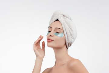 A beautiful woman with blue eyes against a white background, wearing under-eye patches and a towel on her head. Cosmetology ads concept. Healthy, glow skin. Free copy space, banner